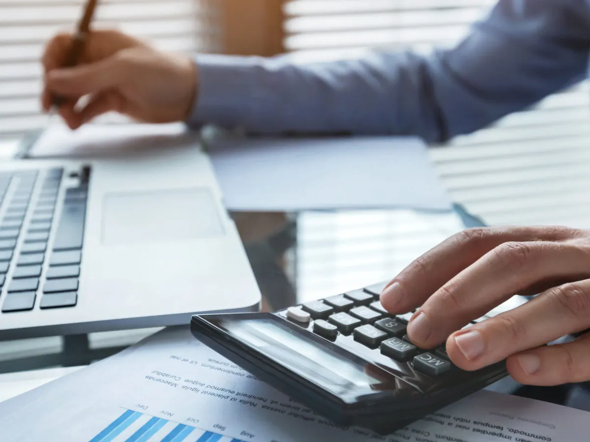 Hände an Taschenrechner und Laptop über einem Finanzbericht